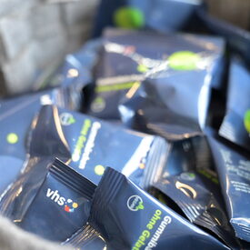 Nahaufnahme eines Korbes mit kleinen blauen Gummibärchen-Packungen, die mit dem vhs-Logo bedruckt sind