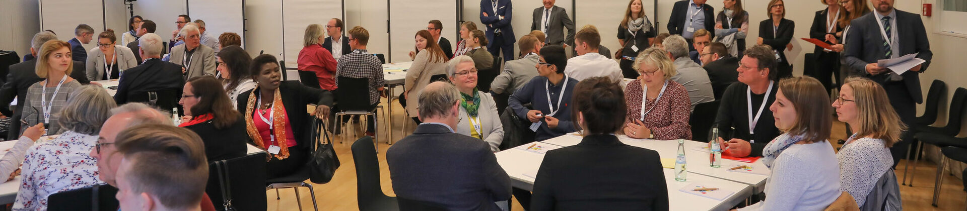 Menschen sitzen an Gruppentischen beim Europadialog der vhs Trier