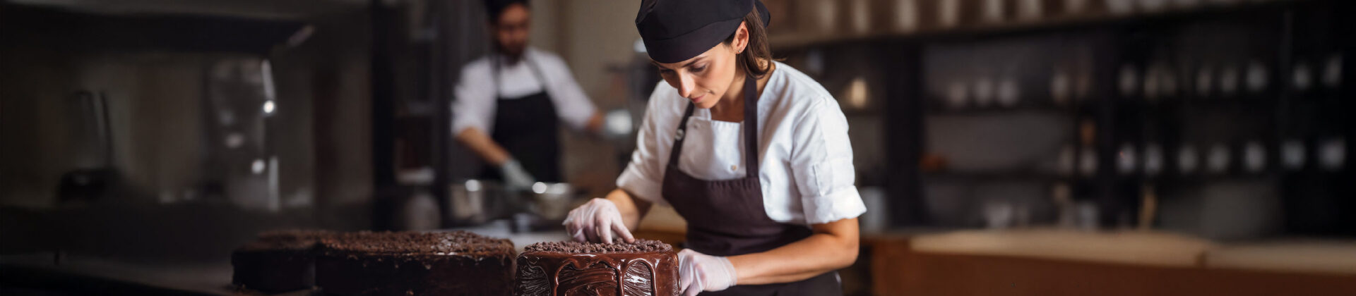 Eine jüngere Frau dekoriert eine Torte mit Schokoüberzug.