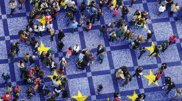 Aufsicht auf mit Menschen gefüllten Platz gepflastert im Stil der Europaflagge