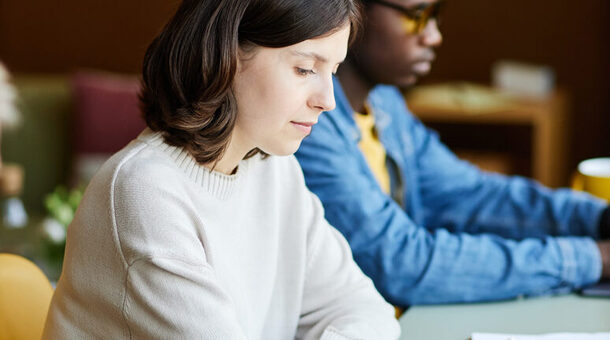 Young Female Corporate Employee Writing in Notebook at Working Desk at Office
