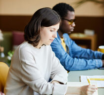 Young Female Corporate Employee Writing in Notebook at Working Desk at Office