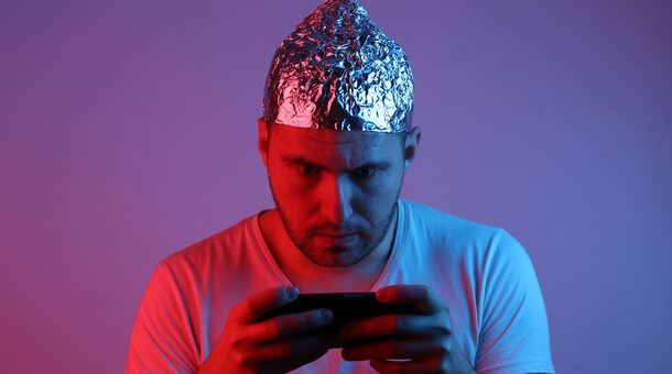 Mann mit Smartphone in der Hand und Aluhut auf dem Kopf