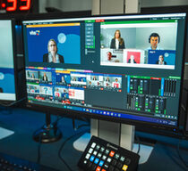 Blick auf mehrere Bildschirme, auf denen einzelne Fenster mit sprechenden Personen und Tonregler zu sehen sind.