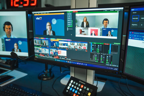 Blick auf mehrere Bildschirme, auf denen einzelne Fenster mit sprechenden Personen und Tonregler zu sehen sind.