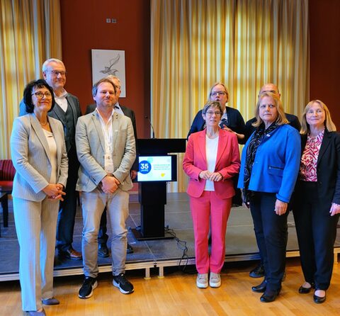 Personengruppe steht zusammen mit einer Bühne und einem Rednerpult im Hintergrund.