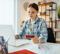 Eine junge Frau sitzt vor einem Laptop, in ihrer linken Hand hält sie eine Bankkarte.