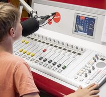 Ein Junge sitzt vor einem Schaltpult und spricht in ein Mikrofon