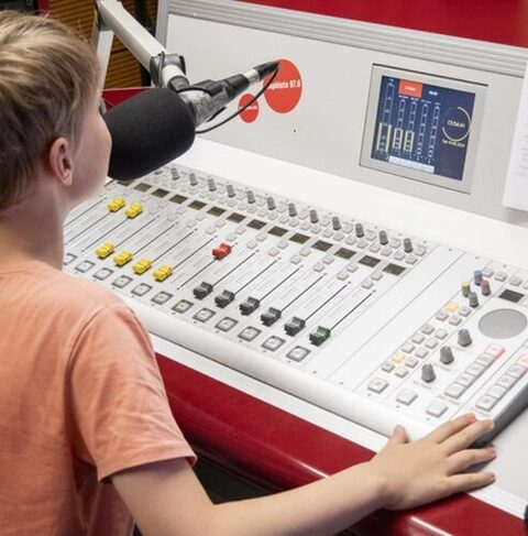 Ein Junge sitzt vor einem Schaltpult und spricht in ein Mikrofon