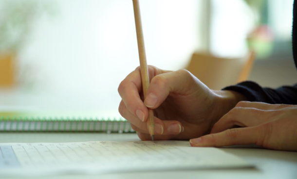 Eine Hand hält einen Stift und schreibt auf einem Arbeitsblatt
