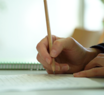 Eine Hand hält einen Stift und schreibt auf einem Arbeitsblatt