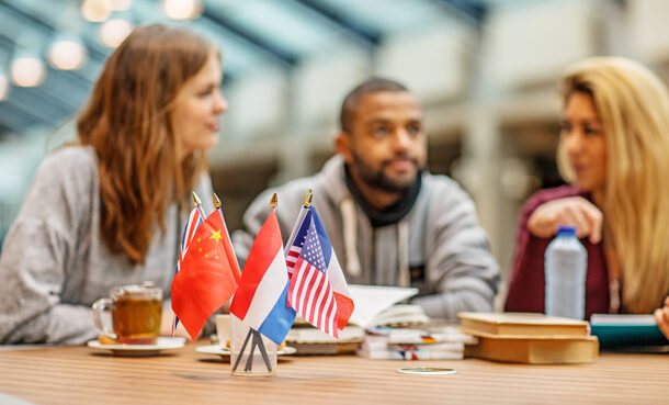 Drei Personen sitzen an einem Tisch, vor ihnen mehrere Landesflaggen.