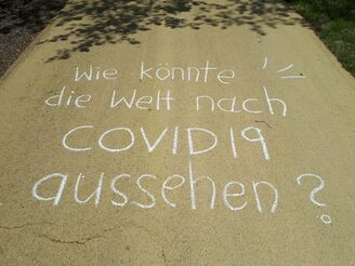 Auf einer Straße steht mit Kreide geschrieben: Wie könnte eine Welt nach COVID19 aussehen?