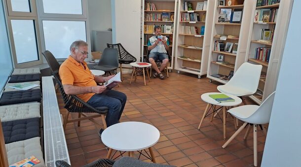 Zwei Personen sitzen auf Stühlen in Raum mit Büchern und lesen.